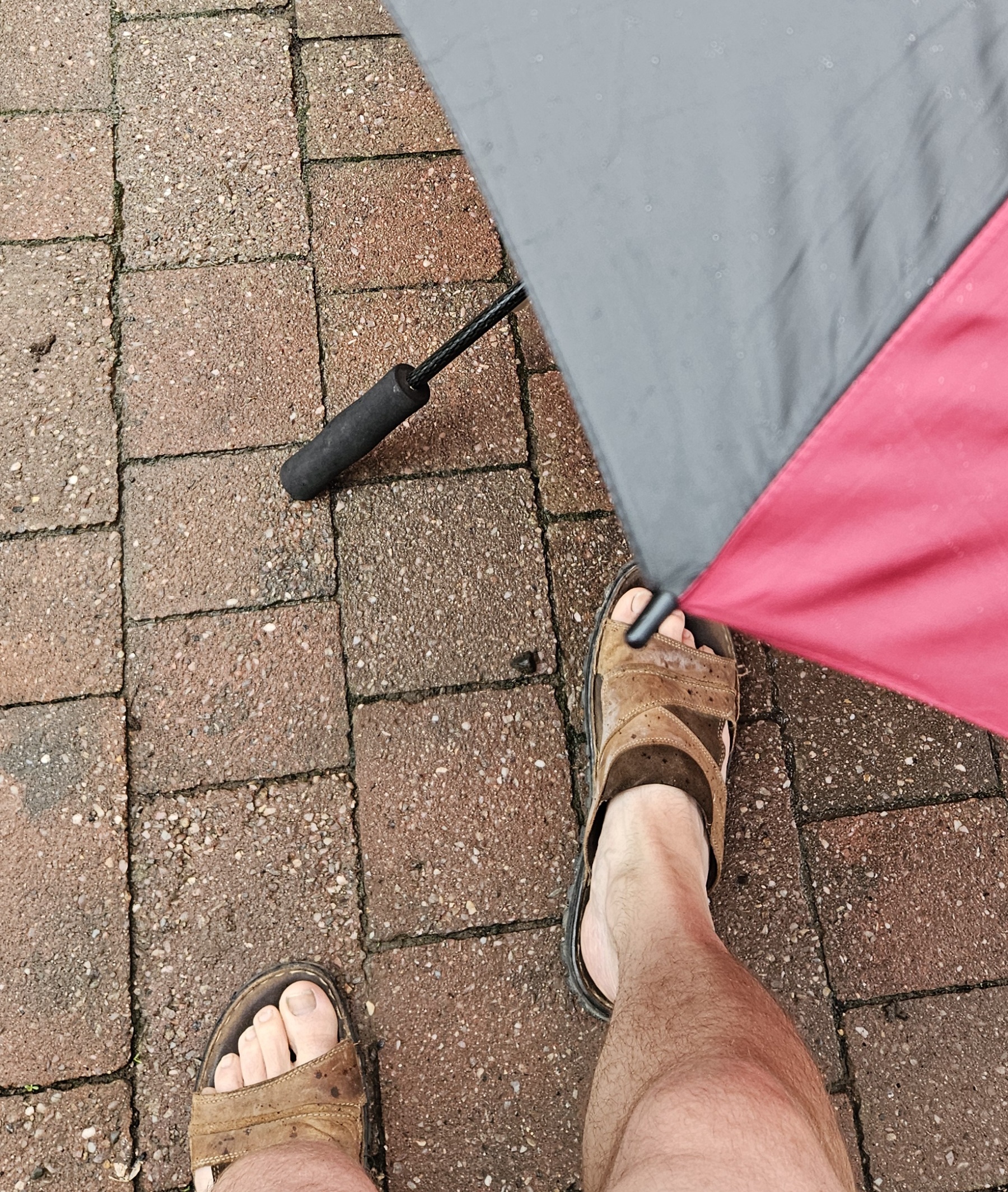 Sandals and an umbrella on a wet brick path